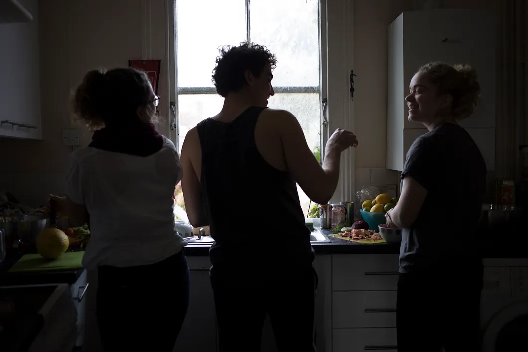 Three people in a kitchen talking and cooking together.